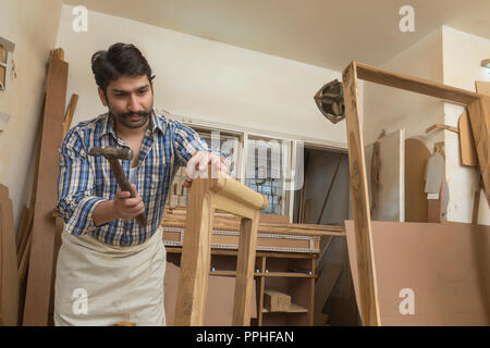 Carpenter hitting a nail on wood with hammer in his workshop. Stock Photo