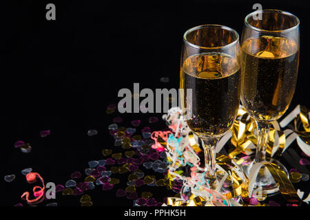 two glasses of champagne on a shiny black surface with confetti against a black background. Stock Photo