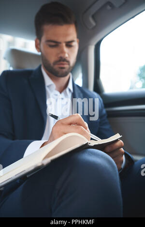 Businessman sitting in car and writing daily plan in his diary Stock Photo