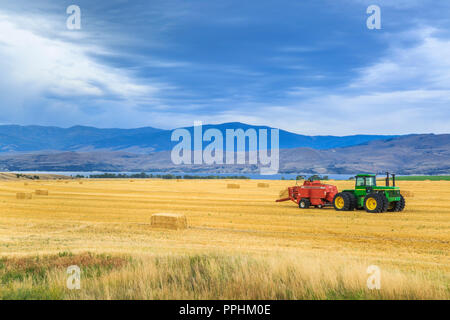 straw bales and tractor in harvested wheat field above canyon ferry lake near townsend, montana Stock Photo