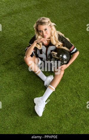 overhead view of young woman in american football uniform holding helmet and looking at camera Stock Photo