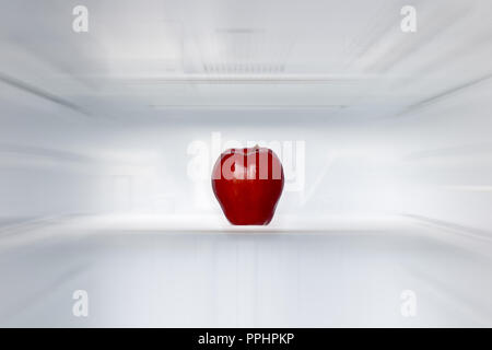 A lone red apple on a shelf in an empty fridge. One fresh apple in an empty clean refrigerator. Fruits is cooling in storage. Stock Photo
