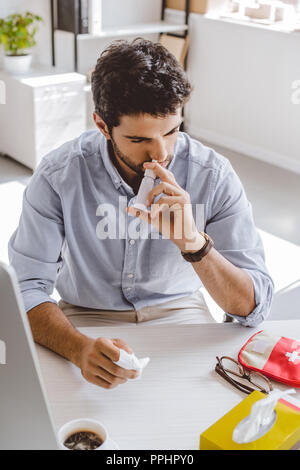high angle view of sick manager using nasal spray in office Stock Photo