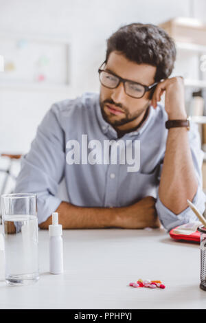 sick manager leaning on table and looking at pills on tabletop in office Stock Photo