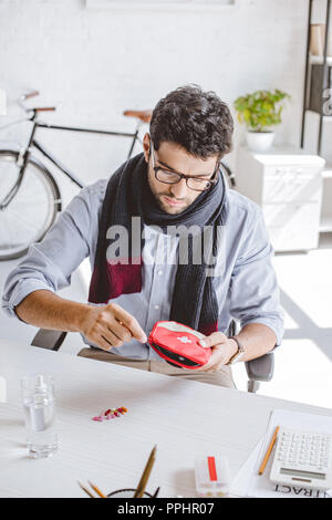 sick businessman in scarf open first aid kit in office Stock Photo