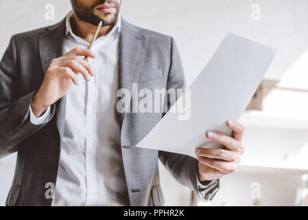 cropped image of businessman reading documents and touching chin with pencil in office Stock Photo