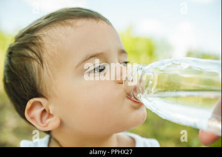 headshot of adorable toddler boy drinking water from plastic bottle in park Stock Photo
