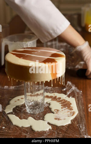 Cheesy mousse cake. Confectioner girl pours a delicate biscuit glaze. Master class in a home sweet shop. Creating a pattern on the surface of the conf Stock Photo