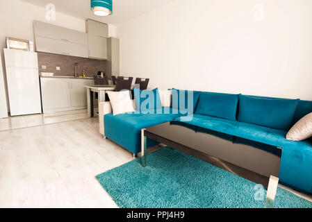 Modern bright and cozy living room interior design with sofa, dining table and kitchen. Grey and turquoise blue studio apartment. Stock Photo