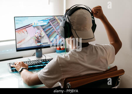 Madrid, Spain - August 15, 2018: Teenager playing Fortnite video game on PC. He is raising his fist in a victory gesture. Fortnite is an online multip Stock Photo