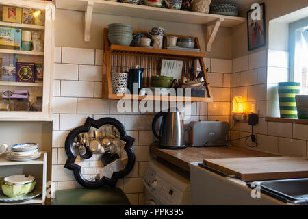 Old fashioned style kitchen with vintage cooking utensils, belfast sink, wooden shelving and mirror against a white brick patterned tiled wall. Stock Photo