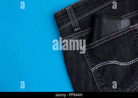 Back pocket of black jeans and black leather wallet on blue background Stock Photo