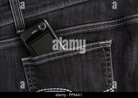 Old (push-button) mobile phone screen up in the back pocket of black jeans Stock Photo