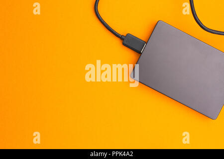 Black external hard disk with USB cable on orange background. Top view. Stock Photo
