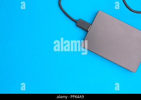 Black external hard disk with USB cable on blue background. Top view. Stock Photo