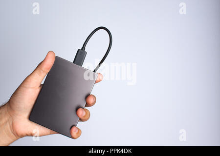 A man's hand holds a portable hard drive on a gray background Stock Photo