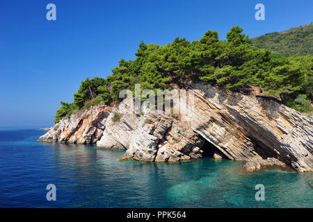 White cliffs, green pine trees in idyllic Petrovac, Montenegro.  Clear blue sky and turquoise transparent ocean water. Stock Photo