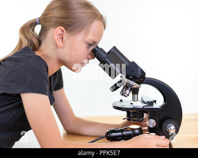 A 9 year old girl looks into an eyepiece of a microscope. Isolated against white background Stock Photo