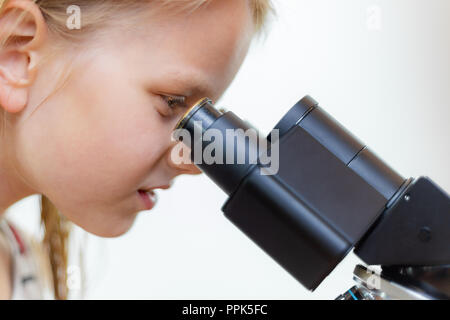 A blond 7 year old schoolchild looks into the eyepiece of a microscope. Isolated Stock Photo