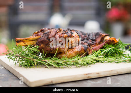 Slow roasted whole lamb shoulder, on a chopping board and a bed of rosemary. Shot outdoors Stock Photo