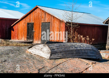 Old broken boat on the wooden sheds for storage of boats in the background. Aland Islands Stock Photo