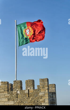 Portuguese flag on the top of the stone wall of a medieval castle fluttering in the wind against the blue sky. Stock Photo