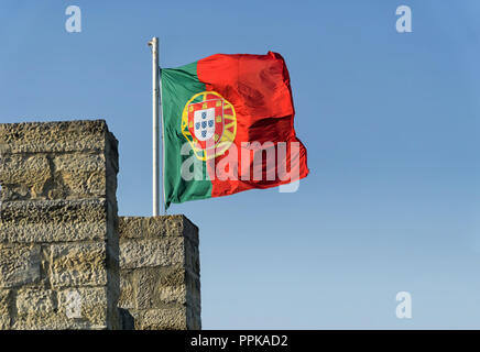 Portuguese flag on the top of the stone wall of a medieval castle fluttering in the wind against the blue sky. Stock Photo