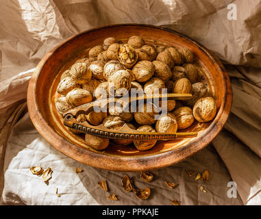 Whole walnuts and cracked walnuts in a vintage clay bowl and a nutcracker with sunlight,close up Stock Photo