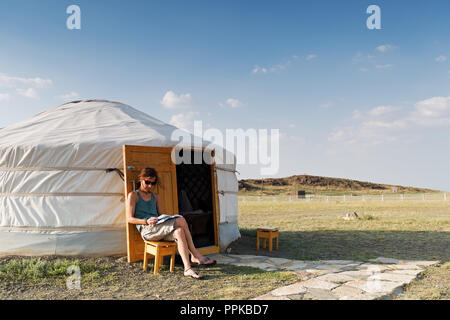 A young women is sitting in front of a mongolian ger in the desert Gobi and is reading a book, Mongolia Stock Photo