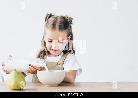 little schoolgirl pouring milk into bowl with breakfast isolated on white Stock Photo