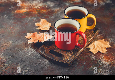 Two colored enamel tea cups, autumn maple leaves on rusty brown background Stock Photo