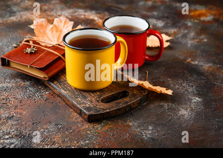 Two colored enamel tea cups, autumn maple leaves on rusty brown background Stock Photo