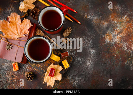 Two colored red and yellow enamel cups of tea, watercolors in cuvettes, colored pencils, autumn maple leaves and bumps on a rusty brown background Stock Photo