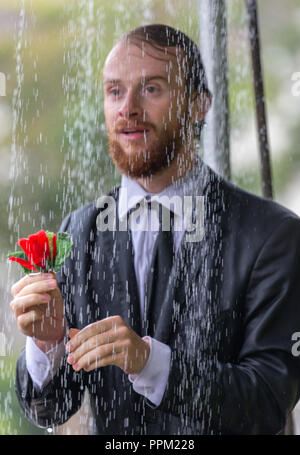 A man waiting in the rain for the woman he loves offers her a single red rose Stock Photo