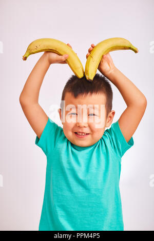 Child boy in turquoise shirt, holds bananas depicting horns - fruit and healthy food Stock Photo