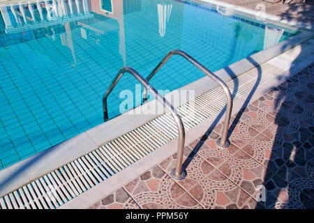 Handrail on the pool. Swimming pool with stair closeup. Pool handrails view. Water swimming pool with sunny reflections. Steel handrail, swimming. Stock Photo