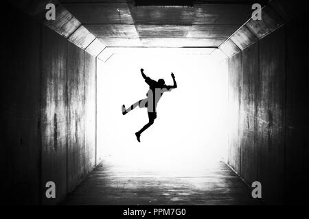 silhouette of a male figure jumping towards the light. graduation happy joy concept or death dying going out with a bang theme. crossing over, jumping Stock Photo