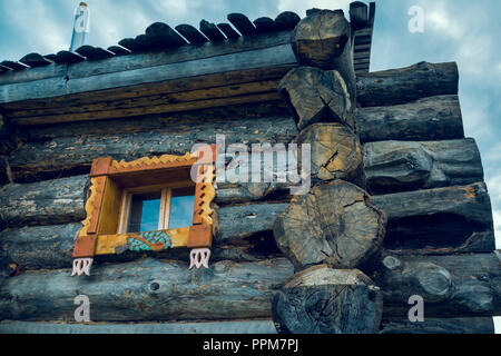 Close-up of a log hut with a window framed by carved platbands against the blue sky Stock Photo