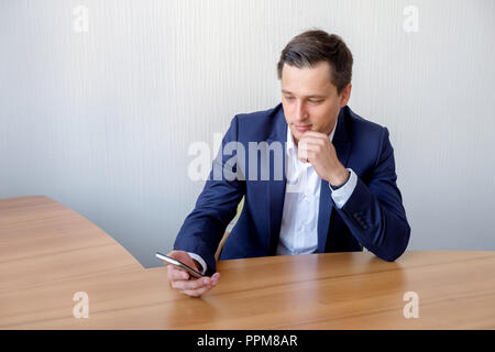 Attractive business man is sitting on his desktop and smiles. Stock Photo