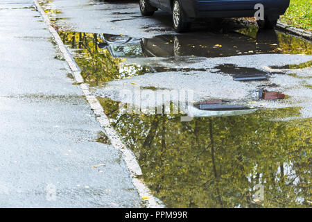 wet asphalt road. water puddles on street sidewalk with parked car Stock Photo