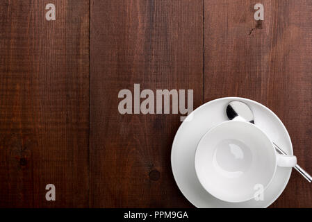 Overhead view of a white porcelain cup saucer and spoon, on a dark wooden table. Stock Photo