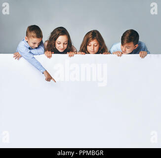 Four children holding a big billboard, looking down on it. Stock Photo