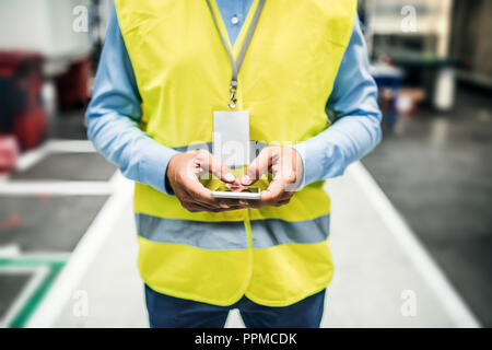 An unrecognizable industrial man engineer with name tag in a factory, using smartphone. Stock Photo