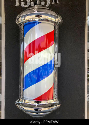 Barber's pole sign attached on the wall in front of a Barber shop. Stock Photo