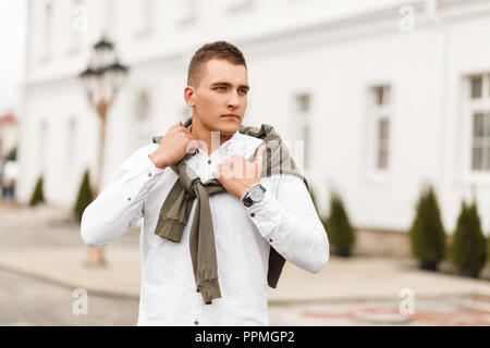 Stylish handsome young successful businessman man in a white shirt with a sweater posing in the city