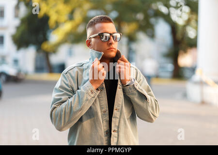 stylish handsome young man with sunglasses and a fashionable denim jacket in the city Stock Photo