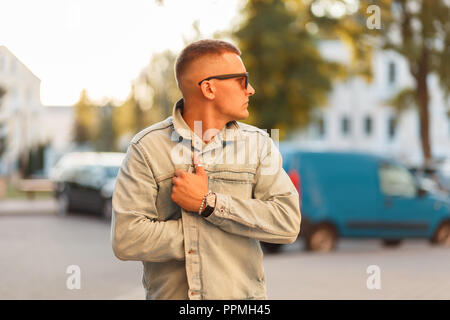 Stylish handsome young man with fashion sunglasses in a denim vintage jacket on a sunny day Stock Photo