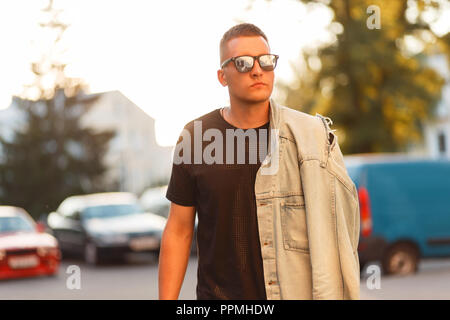 Fashionable man with stylish sunglasses in a black T-shirt and jeans jacket at sunset Stock Photo
