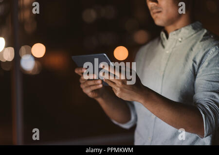 Closeup of a businessman standing in an office late at night using a digital tablet with city lights glowing in the background Stock Photo
