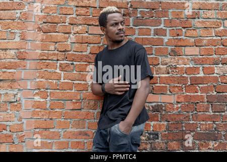 Close up of dark-skinned man in black blank T-shirt on bricked background. Stock Photo